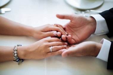 Damat gelini elinden tutar. Yakın plan. Sevgili gelin ve damat bir kafede oturuyor. Çay içiyorum. Aşk, düğün konsepti. Mutlu yeni evli çift