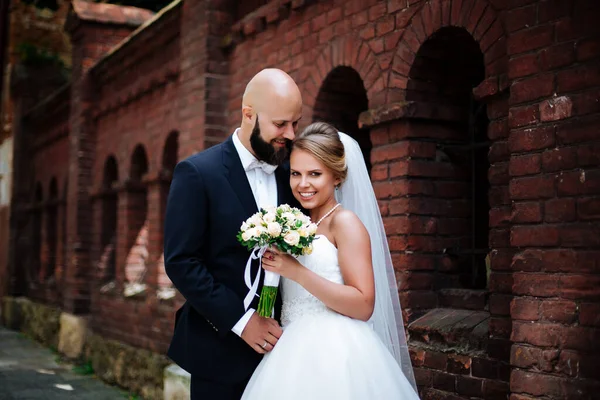 Gelin ve damat tuğla duvarın yanında duruyor. Düğün günü..