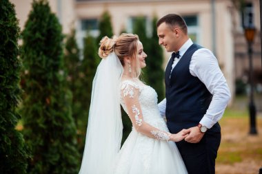 Gelin ve damat parkta birlikte yürürler. Beyaz elbiseli çekici gelin, damat koyu renkli şık bir takım giyiyor.