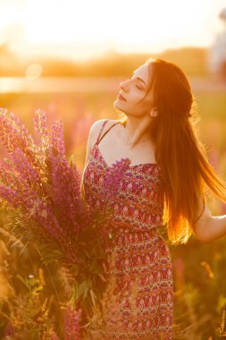 Çiçek tarlasında elinde mor luplu büyük bir çiçek tutan güzel bir kız. Çiçek açan lupin çiçekleri