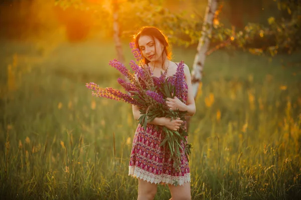 Young girl stand in field overlooking lavender field. Smiling carefree caucasian girl in dress enjoying the sunset.