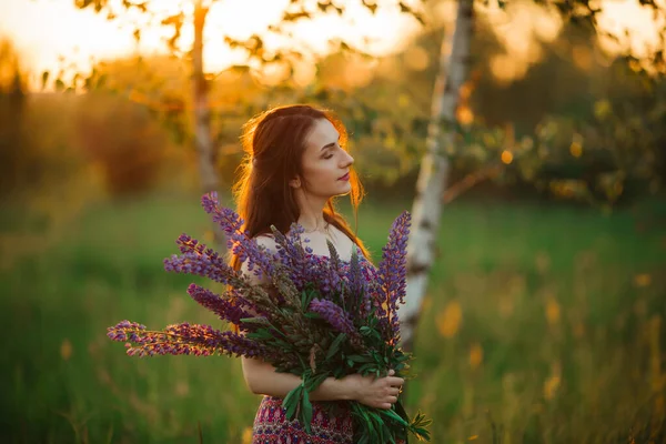 Young girl stand in field overlooking lavender field. Smiling carefree caucasian girl in dress enjoying the sunset.