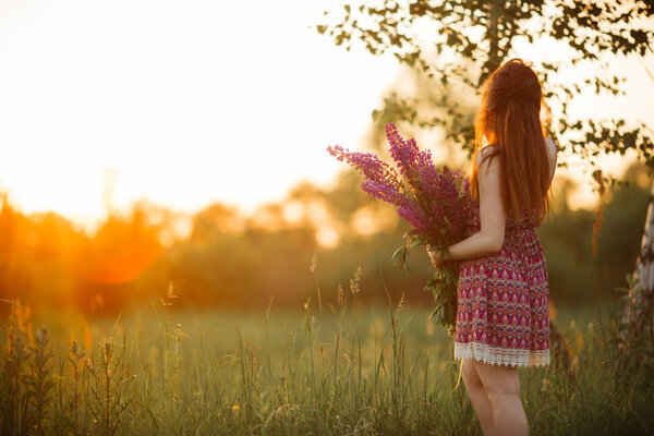 Beautiful girl in a lupine field. Girl holding a bouquet of lupines.