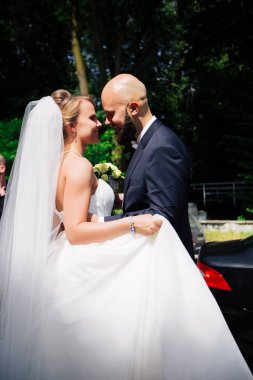 Genç ve güzel bir gelin ve kocası bir buket çiçekle bir yaz parkında dikiliyor..