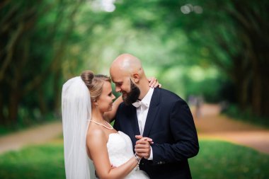 Düğün çifti, güzel genç gelin ve damat parkta el ele tutuşup gülümsüyorlar..