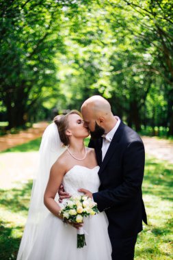 Genç ve güzel bir gelin ve kocası bir buket çiçekle bir yaz parkında dikiliyor..