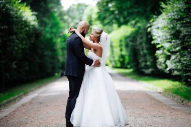 Genç ve güzel bir gelin ve kocası bir buket çiçekle bir yaz parkında dikiliyor..