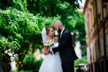 Genç ve güzel bir gelin ve kocası bir buket çiçekle bir yaz parkında dikiliyor..