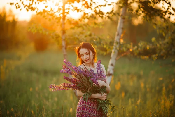 日落时 一个漂亮的年轻女子在田野里 抱着花 — 图库照片