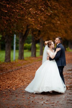 Gelin ve damat parkta birlikte yürürler. Beyaz elbiseli çekici gelin, damat koyu renkli şık bir takım giyiyor.