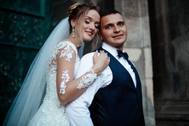 Gelin ve damat parkta birlikte yürürler. Beyaz elbiseli çekici gelin, damat koyu renkli şık bir takım giyiyor.
