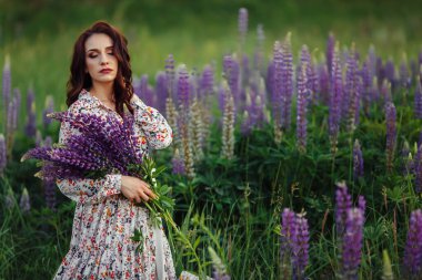 Güzel esmer, elinde lupin çiçekleri, akşam makyajı.