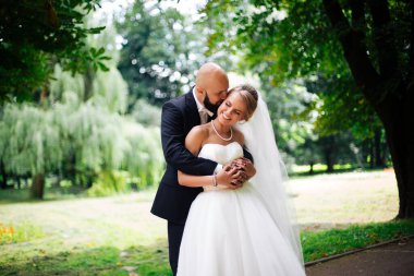 Genç ve güzel bir gelin ve kocası bir buket çiçekle bir yaz parkında dikiliyor..