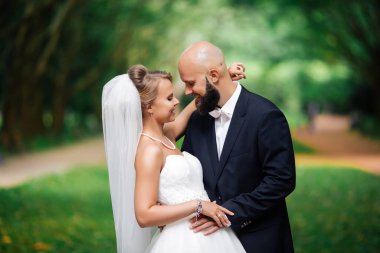 Düğün çifti, güzel genç gelin ve damat parkta el ele tutuşup gülümsüyorlar..