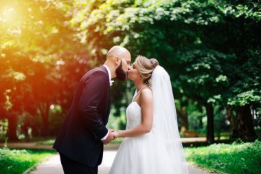 Düğün çifti, güzel genç gelin ve damat parkta el ele tutuşup gülümsüyorlar..