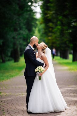 Genç ve güzel bir gelin ve kocası bir buket çiçekle bir yaz parkında dikiliyor..