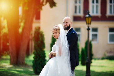 Genç ve güzel bir gelin ve kocası bir buket çiçekle bir yaz parkında dikiliyor..