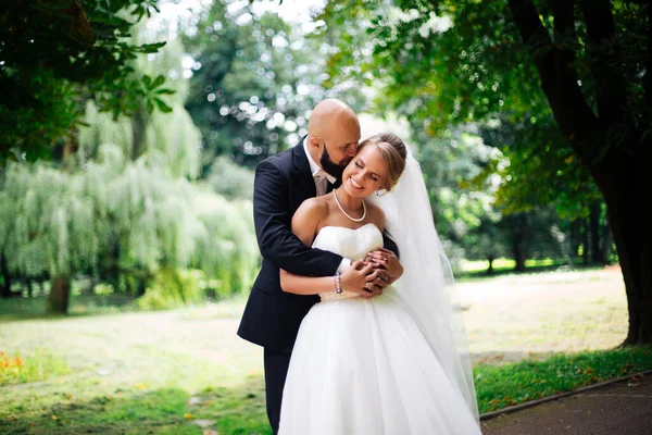 Genç ve güzel bir gelin ve kocası bir buket çiçekle bir yaz parkında dikiliyor..