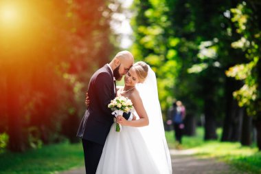 Düğün çifti, güzel genç gelin ve damat parkta el ele tutuşup gülümsüyorlar..