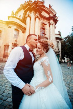 Gelin ve damat parkta birlikte yürürler. Beyaz elbiseli çekici gelin, damat koyu renkli şık bir takım giyiyor.