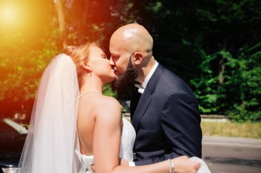 Genç ve güzel bir gelin ve kocası bir buket çiçekle bir yaz parkında dikiliyor..