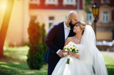 Genç ve güzel bir gelin ve kocası bir buket çiçekle bir yaz parkında dikiliyor..