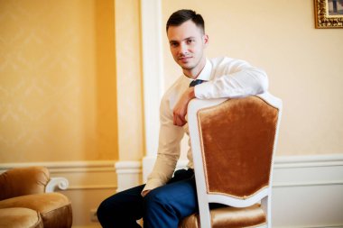 Tişörtlü damat oteldeki sandalyede oturuyor..