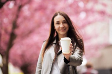 Sakura arka planında bir fincan kahve için poz veren bir kız. Sakura yakınlarında esmer bir kadın.