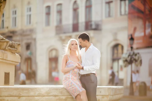 Mooi stel dat een blokje om loopt. donkerharige man in een wit shirt knuffelen een blonde in een mooie jurk — Stockfoto