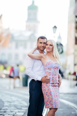 Birbirine aşık genç bir çift şehrin arka planında birbirlerine sarılıyorlar.