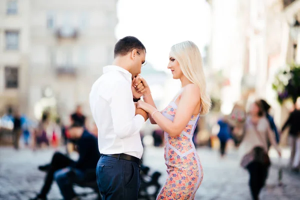 Um lindo casal a passear pelo quarteirão. Homem de cabelos escuros em uma camisa branca abraçando uma loira em um vestido bonito — Fotografia de Stock