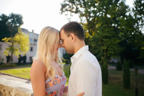 Una bella coppia che gira per l'isolato. Uomo dai capelli scuri in camicia bianca che abbraccia una bionda in un bellissimo vestito — Foto Stock