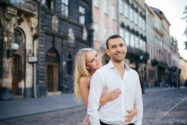 Schönes Paar, das um den Block geht. Dunkelhaariger Mann in weißem Hemd umarmt eine Blondine in einem schönen Kleid — Stockfoto