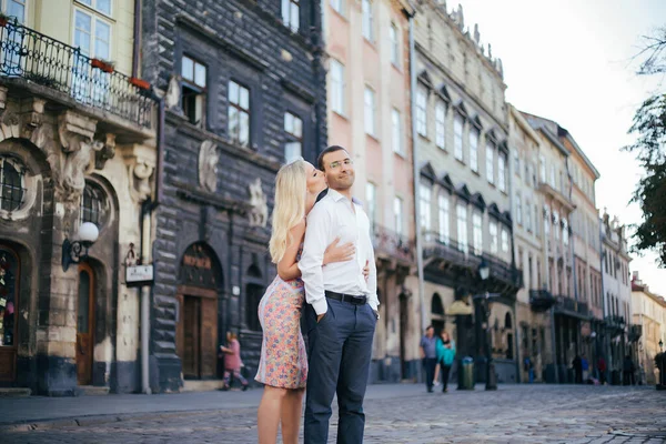 Schönes Paar, das um den Block geht. Dunkelhaariger Mann in weißem Hemd umarmt eine Blondine in einem schönen Kleid — Stockfoto