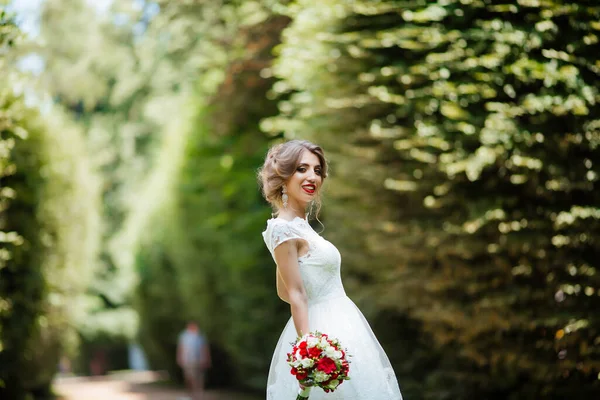 Brunetka panna młoda w sukience z bukietem ślubnym w parku na tle zieleni — Zdjęcie stockowe