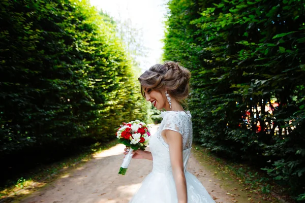 Hermosa novia con un ramo de bodas en sus manos al aire libre en el parque . — Foto de Stock