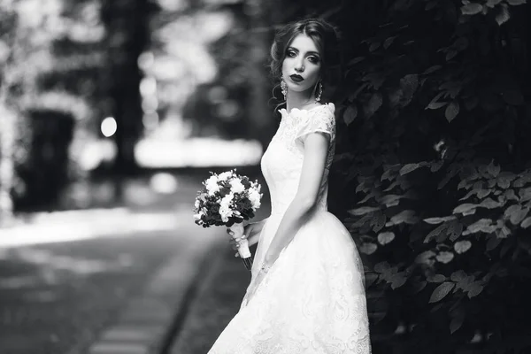 Die Braut im weißen Brautkleid hält einen Strauß vor einem grünen Park — Stockfoto