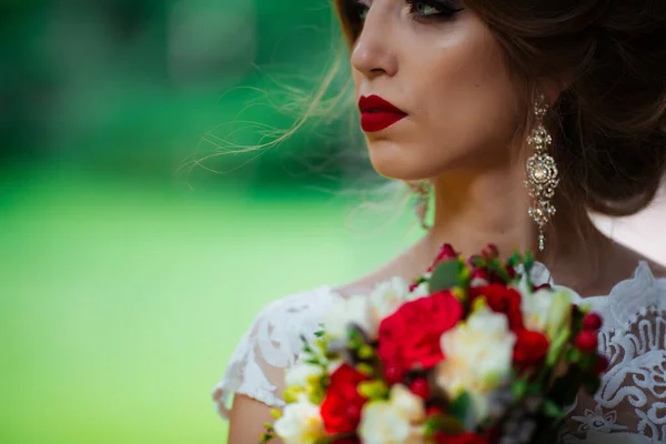 Bela noiva com um buquê de casamento em suas mãos ao ar livre no parque . — Fotografia de Stock