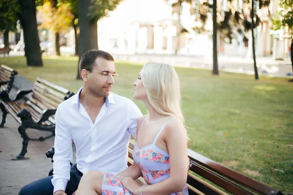 Um lindo casal a passear pelo quarteirão. Homem de cabelos escuros em uma camisa branca abraçando uma loira em um vestido bonito — Fotografia de Stock