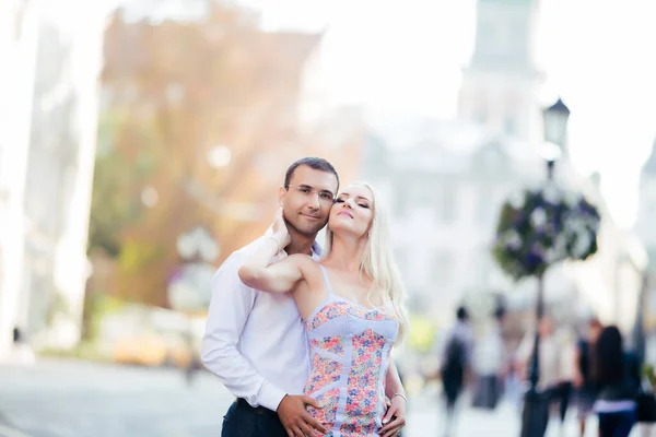 Härligt par som går runt kvarteret. Mörkhårig man i vit skjorta kramar en blondin i vacker klänning — Stockfoto