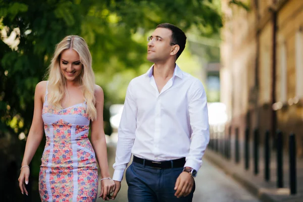 Charmant couple marchant autour du pâté de maisons. Homme aux cheveux bruns dans une chemise blanche embrassant une blonde dans une belle robe — Photo