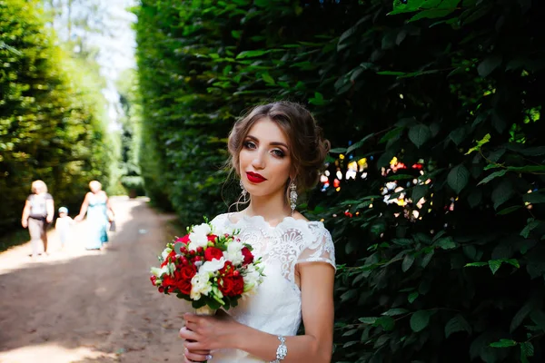 Brünette Braut im Kleid mit Brautstrauß im Park vor grünem Hintergrund — Stockfoto