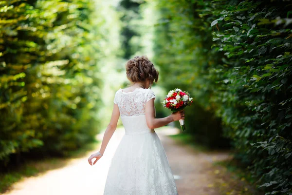 Schöne Braut mit einem Brautstrauß in der Hand im Freien im Park. — Stockfoto