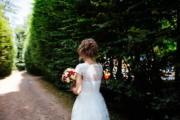 Schöne Braut mit einem Brautstrauß in der Hand im Freien im Park. — Stockfoto
