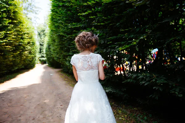 Наречена в білій весільній сукні тримає букет на фоні зеленого парку — стокове фото