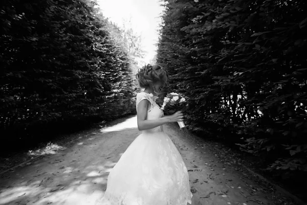 A menyasszony fehér esküvői ruhában egy csokrot tart a zöld park hátterében. — Stock Fotó
