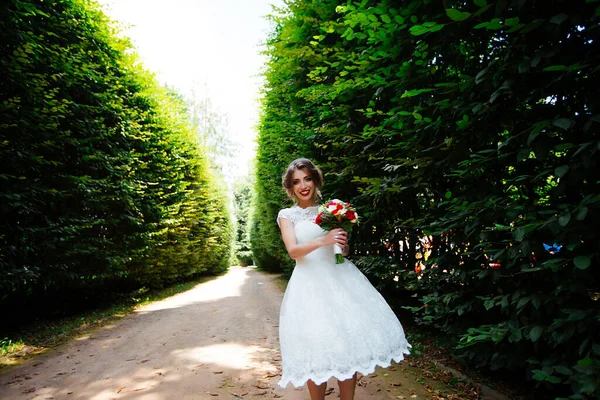 Brünette Braut im Kleid mit Brautstrauß im Park vor grünem Hintergrund — Stockfoto