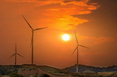 Dağlık arazideki rüzgar türbinleri günbatımına karşı arka planda bulutlar, elektrik enerjisi konsepti için yel değirmenleri