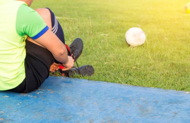Saha kenarına futbol ayakkabısı bağlayan Asyalı genç sporcu, sahada oynamaya hazır erkek futbol, sağlık ve spor konsepti.