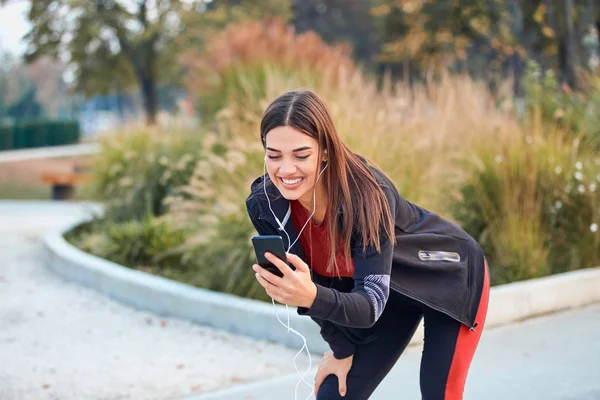 Modern young woman with cellphone making pause during jogging / — Zdjęcie stockowe